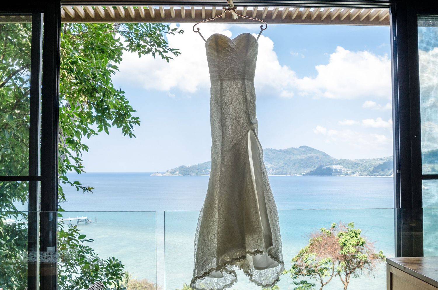 Wedding gown hung on a big glass window overlooking a tropical beach taken by a Melbourne couples, engagement and wedding photographer.
