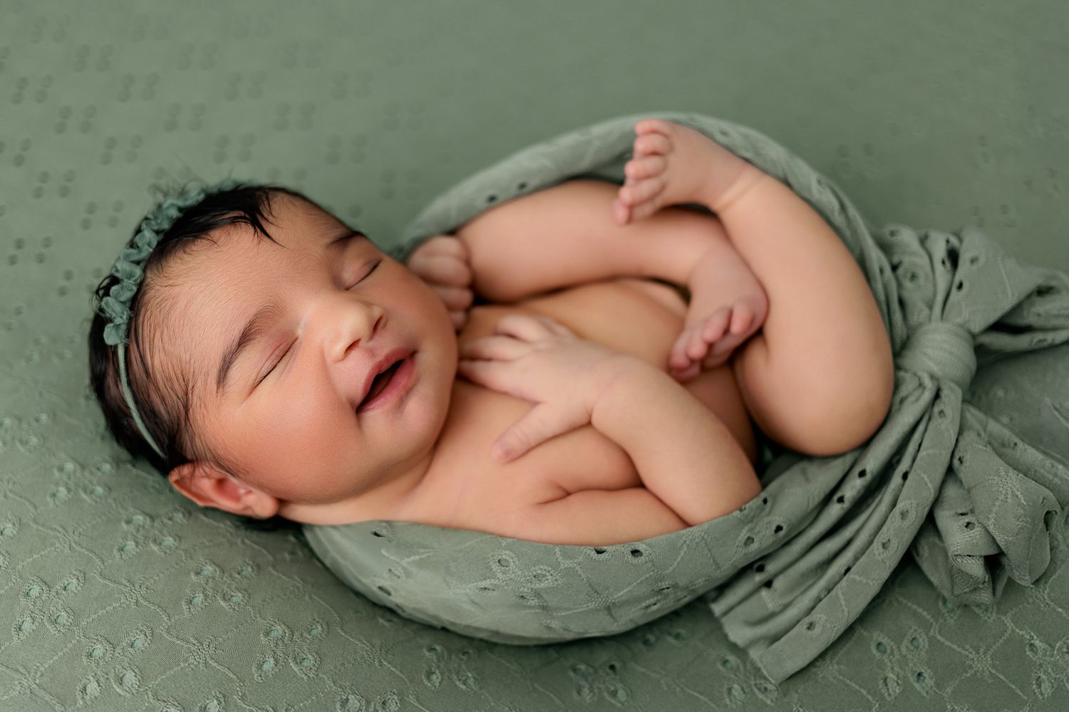 Newborn baby sleeping peacefully wrapped in soft green fabric during professional photo session in Cedar Park Tx.