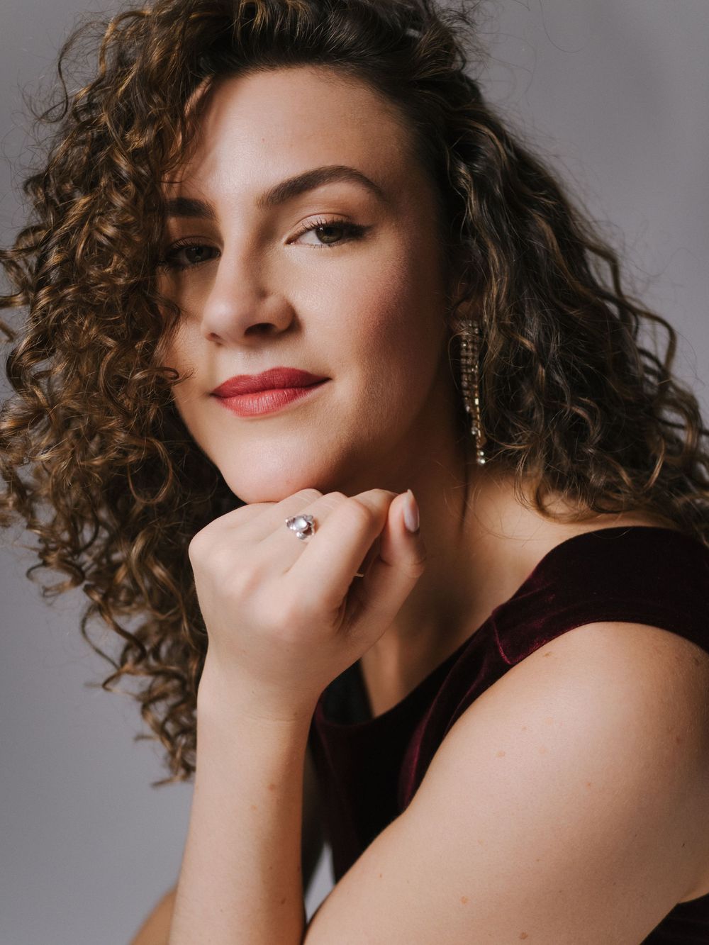 Portrait of a woman with curly brown hair and red lipstick posing against a gray background in four similar poses.