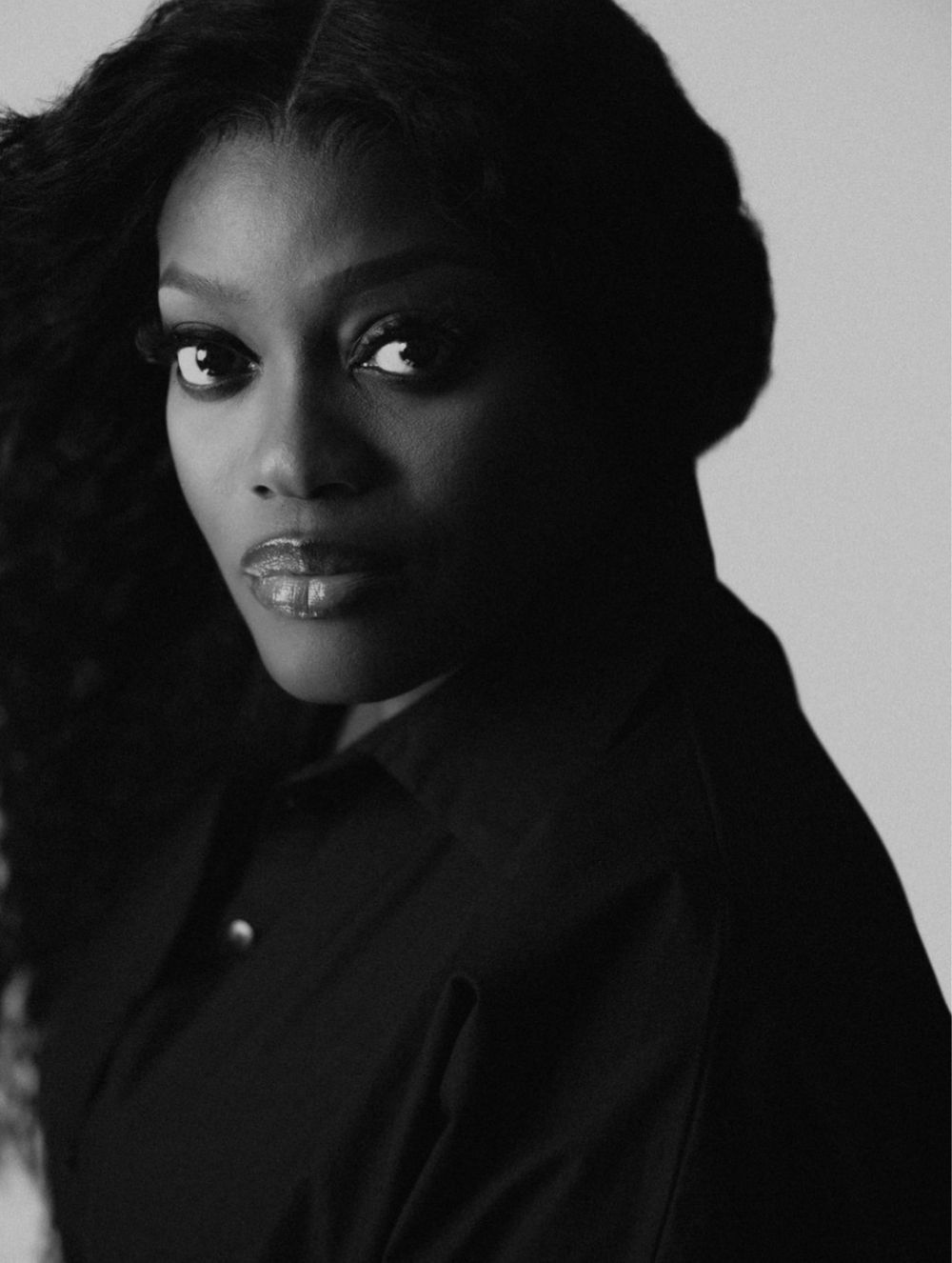 Dramatic black and white portrait featuring striking eyes and dark hair against a shadowy background.