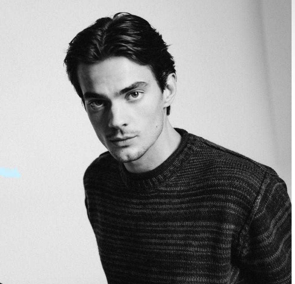 Black and white portrait photo of a person in a dark turtleneck sweater against a light background.
