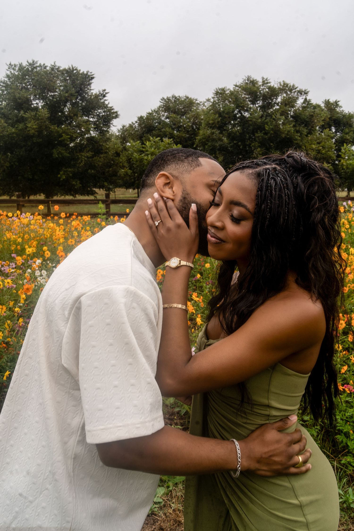 A couple shares a tender moment in a colorful wildflower field, the woman in green holding his face gently.