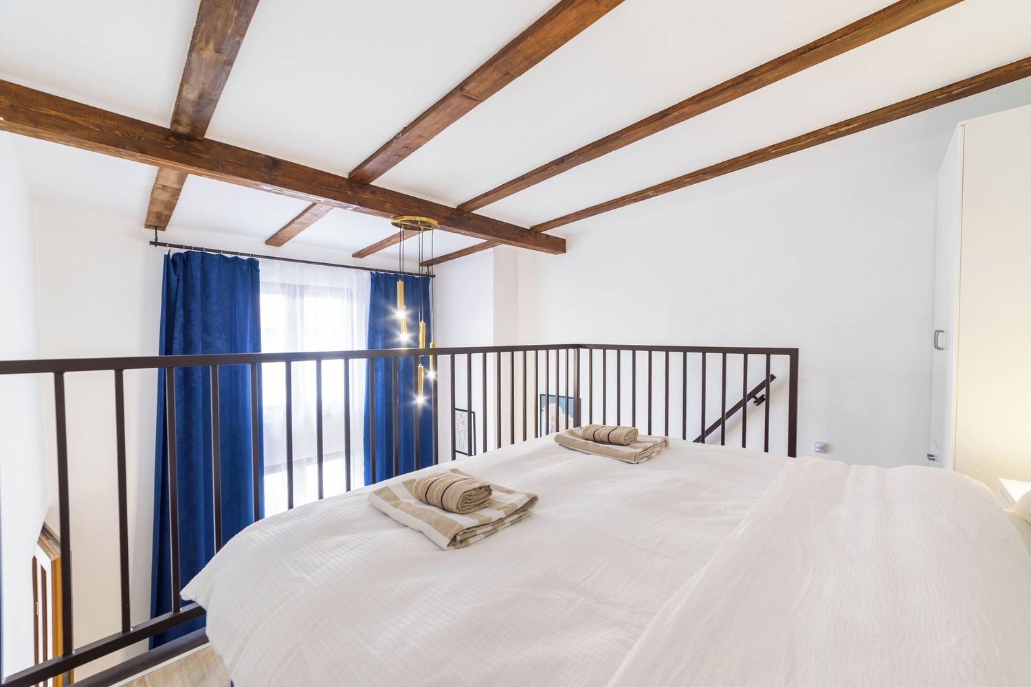Modern loft bedroom interior with exposed wooden beams, white walls and blue curtains creating an airy atmosphere.