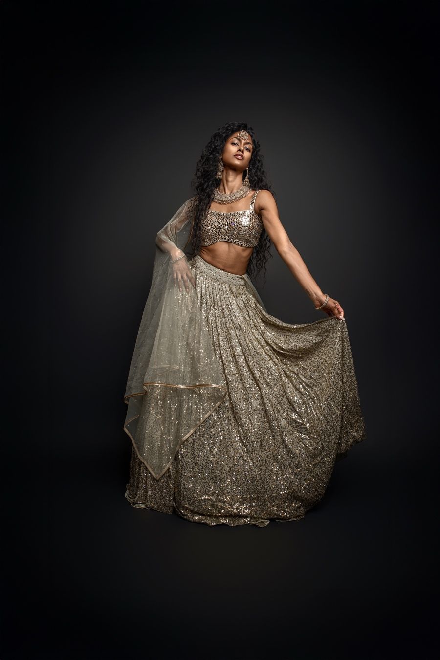 A model in a sparkling gold evening gown poses dramatically against a dark background in a fashion photoshoot series.