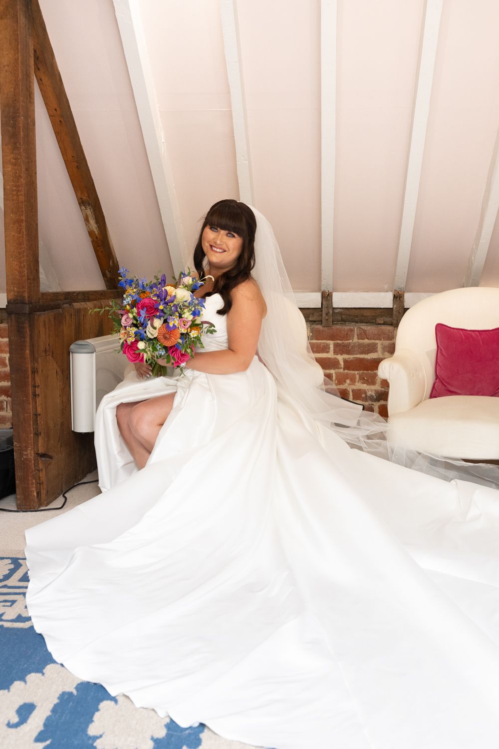 A bride in a flowing white wedding gown lounges on a luxurious white bed with colorful floral accents.