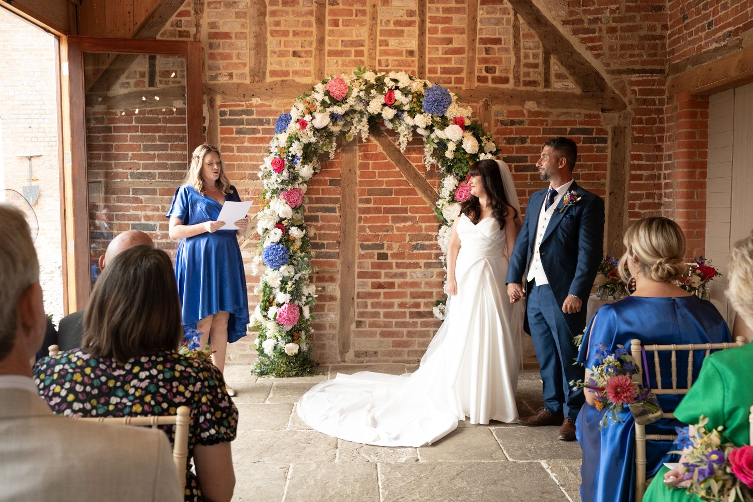 Wedding ceremony in progress inside historic brick loft space decorated with floral arrangements and blue accents.