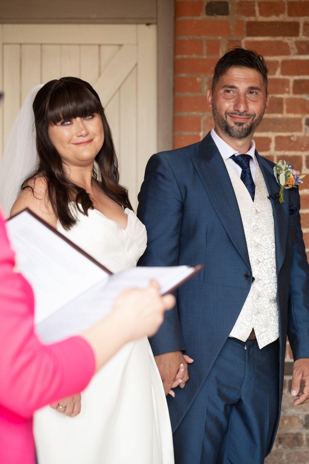 Wedding party poses against a rustic brick wall with white doors in formal attire.