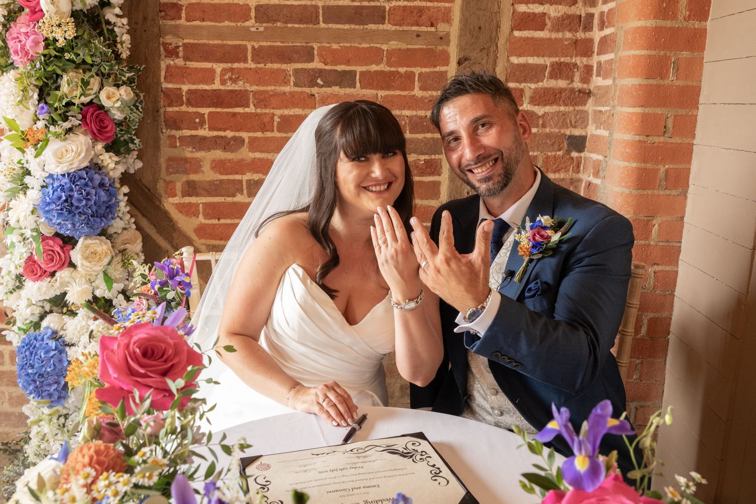A couple celebrates joyfully at their wedding ceremony under an elegant floral arch with colorful blooms.