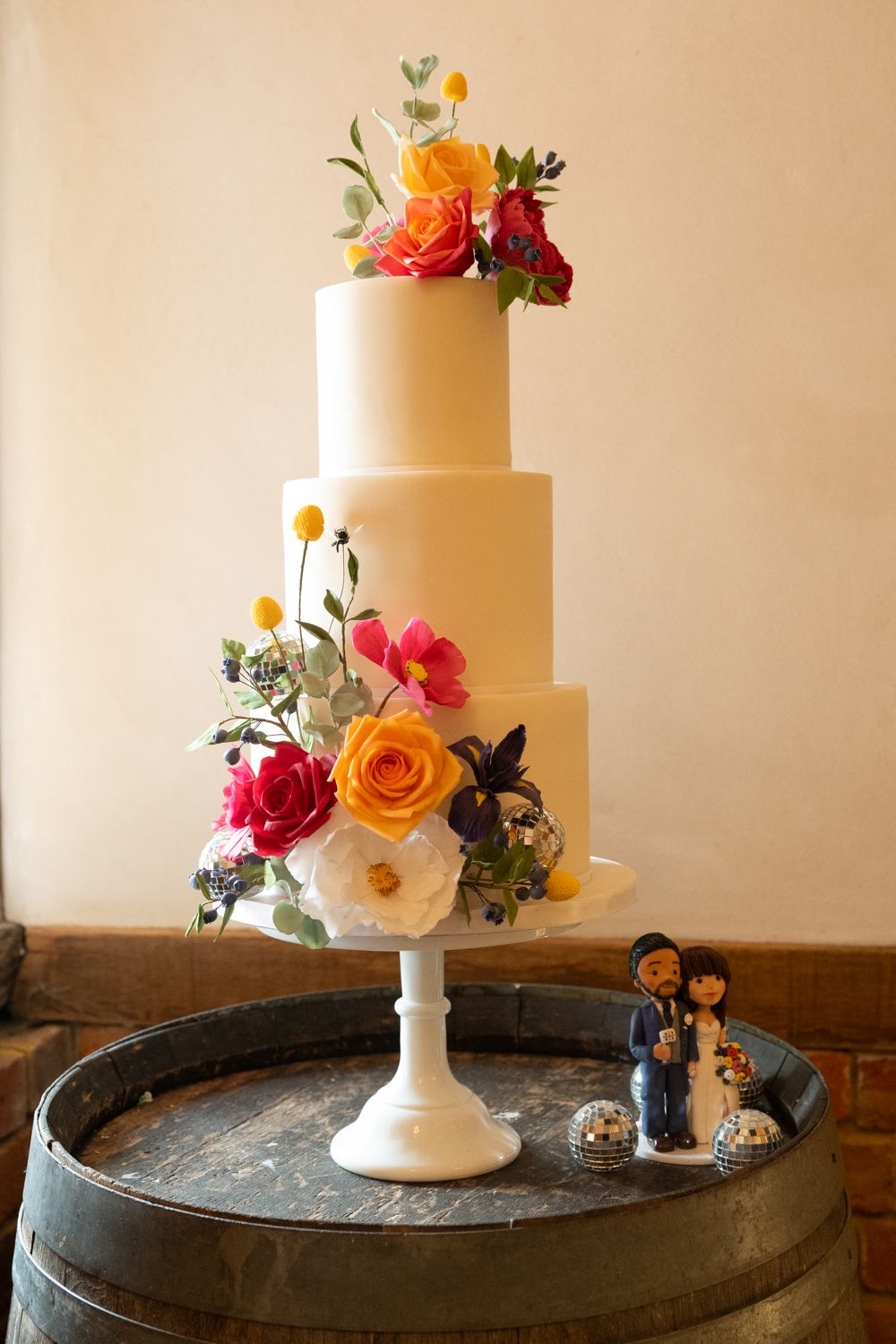 Elegant three-tier white wedding cake adorned with fresh orange and pink flowers displayed on a vintage pedestal stand.