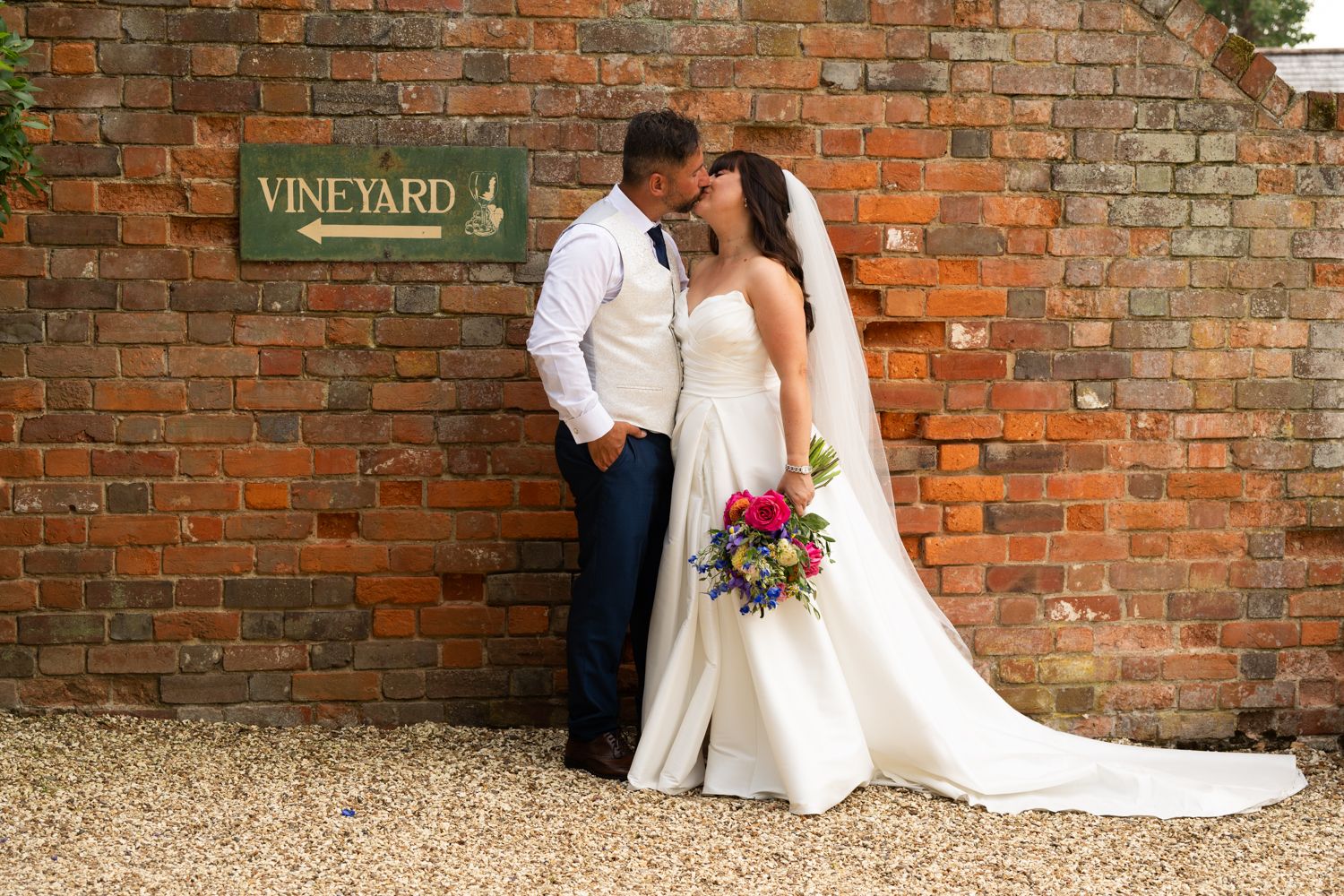A bride and groom share intimate moments against rustic brick walls at a vineyard wedding venue.