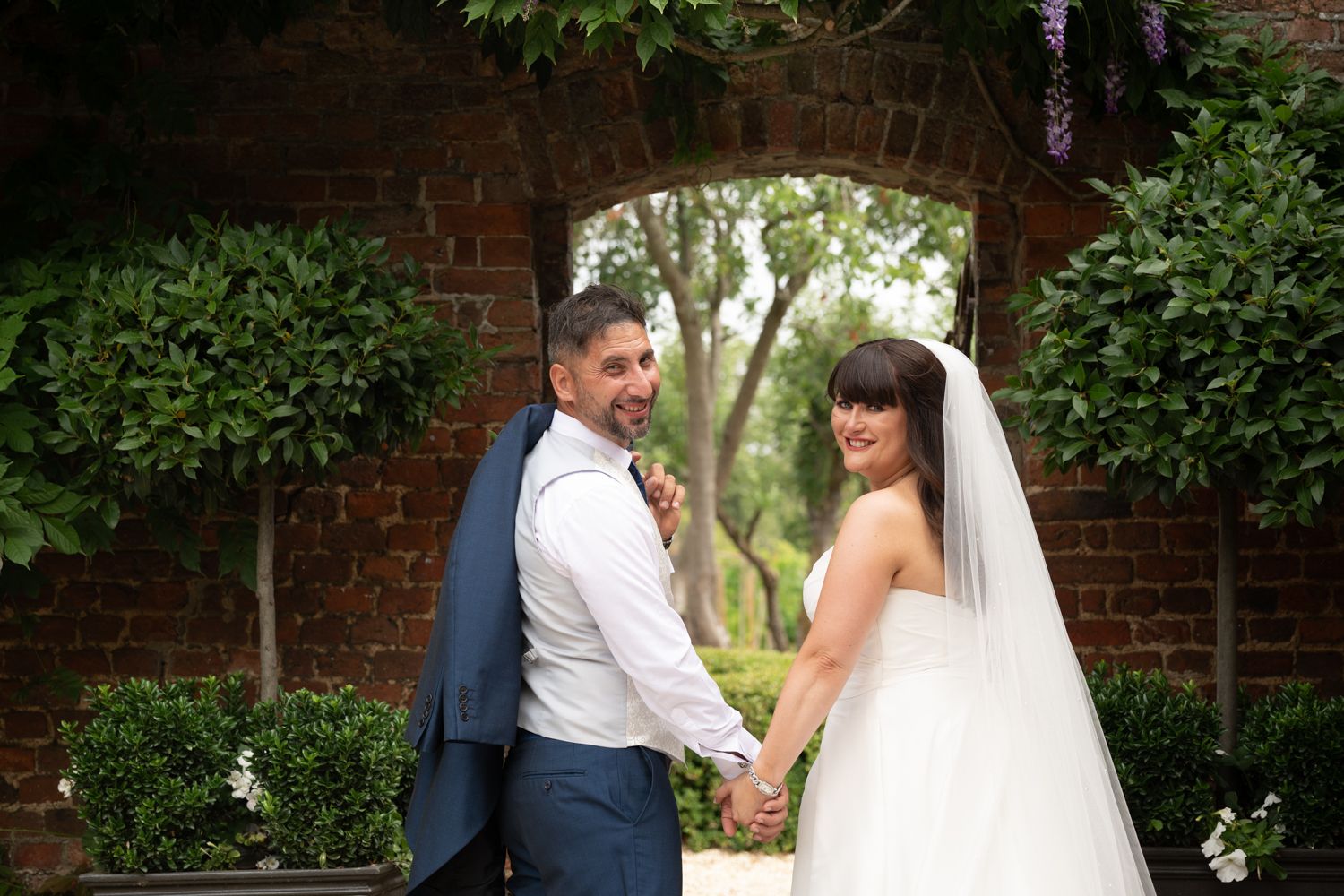 Romantic wedding couple shares intimate moments in a garden setting with brick walls and lush greenery.