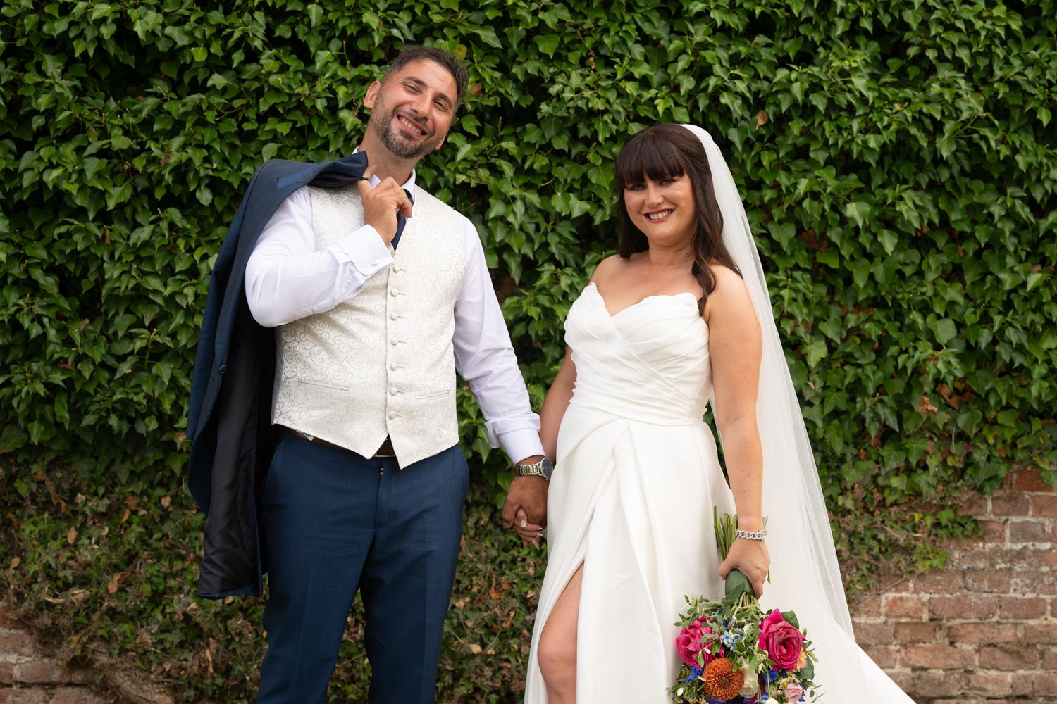 Newlyweds share a romantic moment in front of lush green hedges at an outdoor wedding venue.