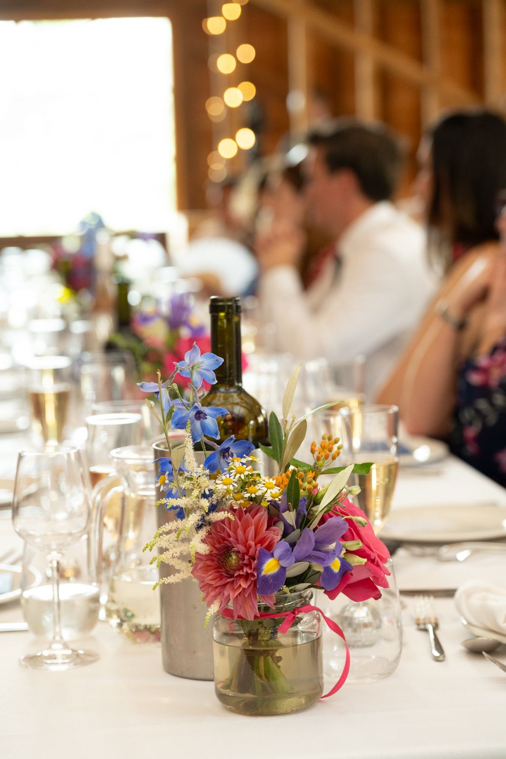 Elegant wedding table centerpieces featuring pink and purple flowers in glass jars with white linens.
