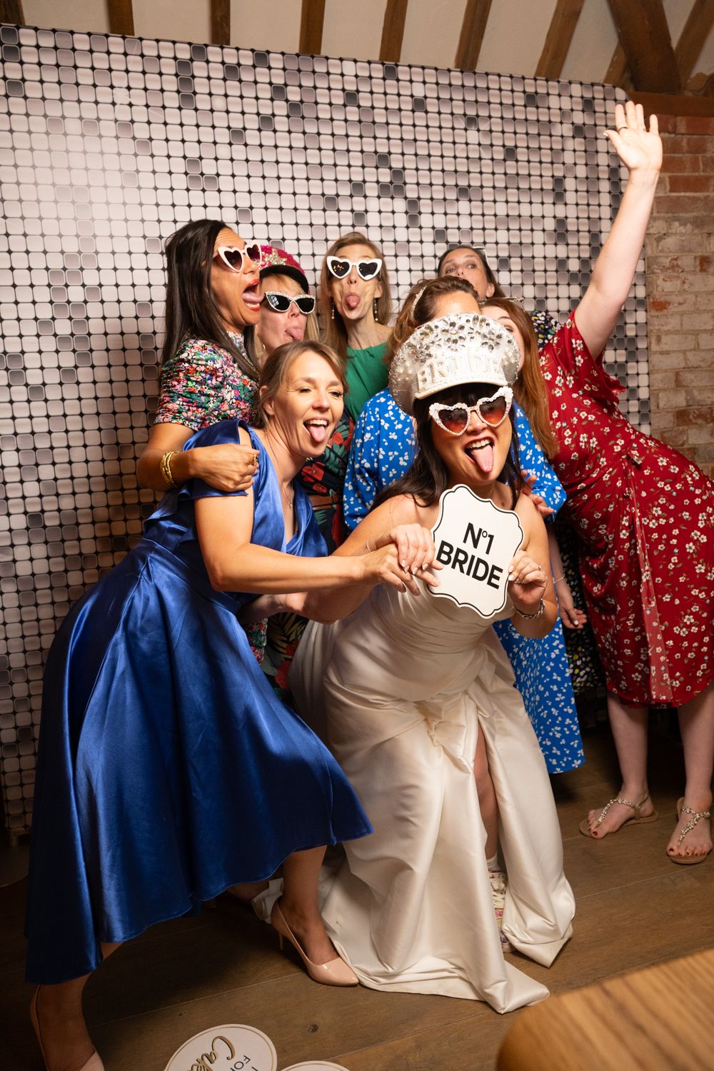 A lively group poses with props and sunglasses against a sparkly backdrop at a wedding celebration party.