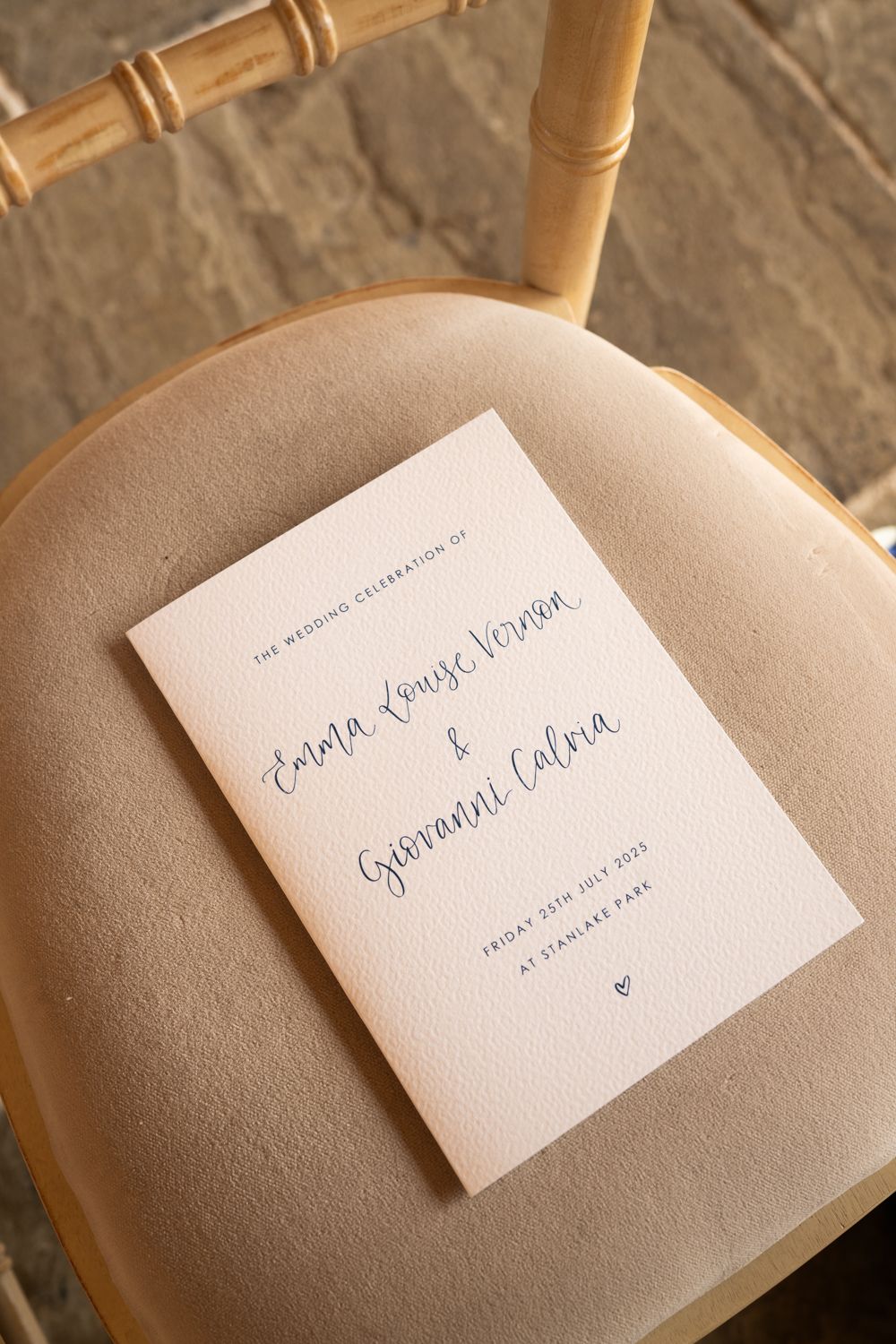 A series of wedding place cards in elegant calligraphy handwriting shown on a beige chair cushion.
