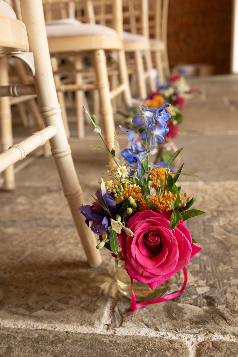 Small colorful floral boutonnieres with pink roses and blue flowers arranged in a row on a rustic surface.