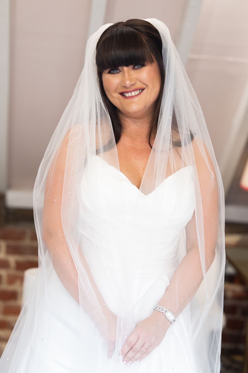 A bride in a white wedding dress and long veil smiles while posing for a portrait.