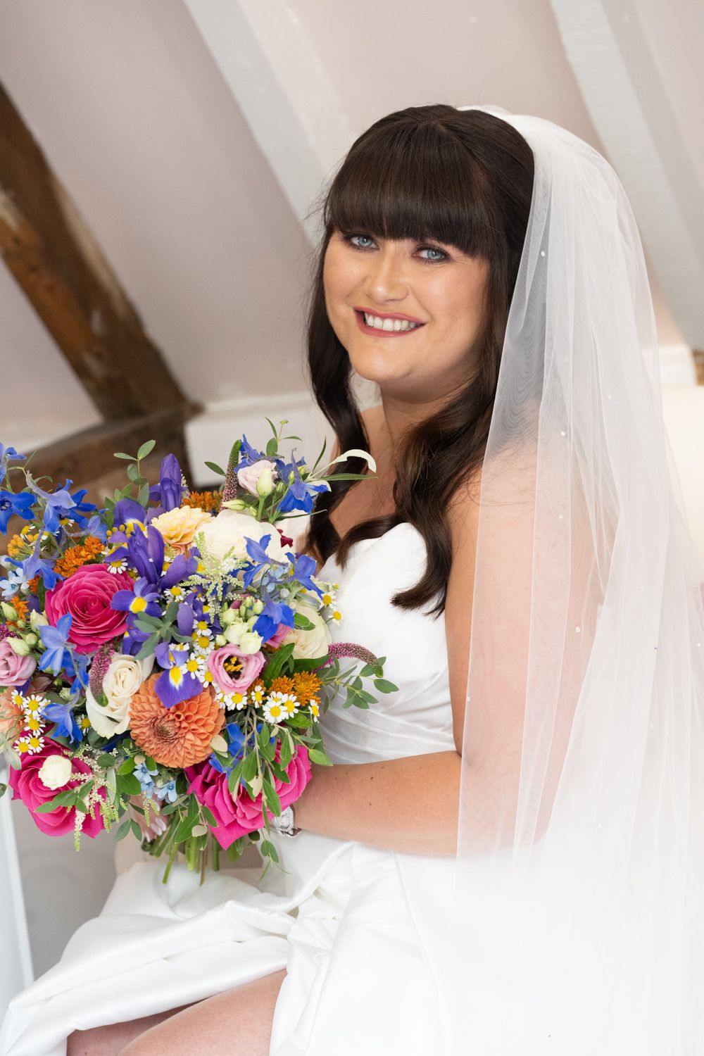 Colorful wedding bouquet with vibrant pink, blue and orange flowers held by bride in white dress and veil.