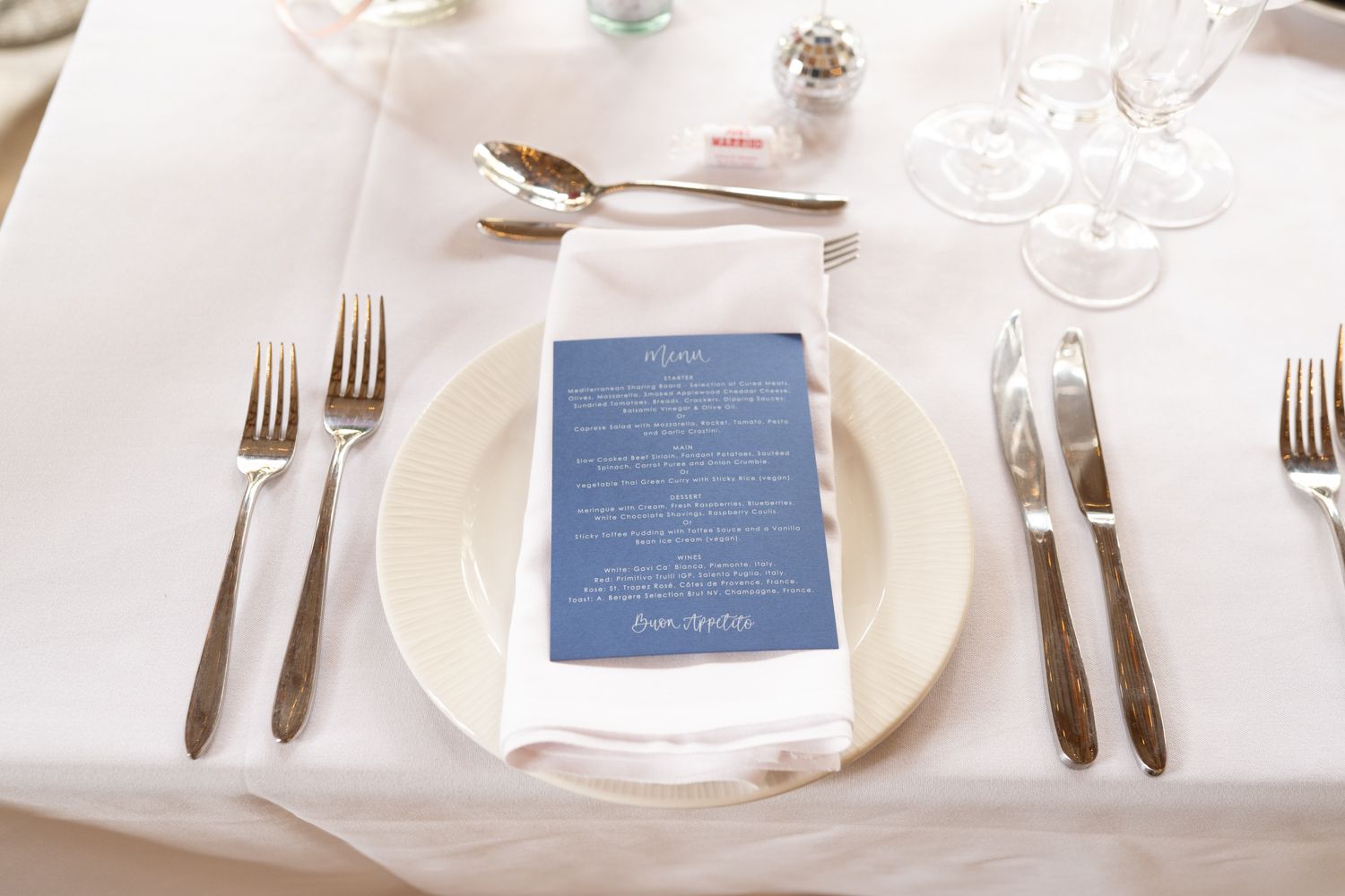 A formal place setting with white plate, navy blue menu card, and polished silverware on crisp white tablecloth.