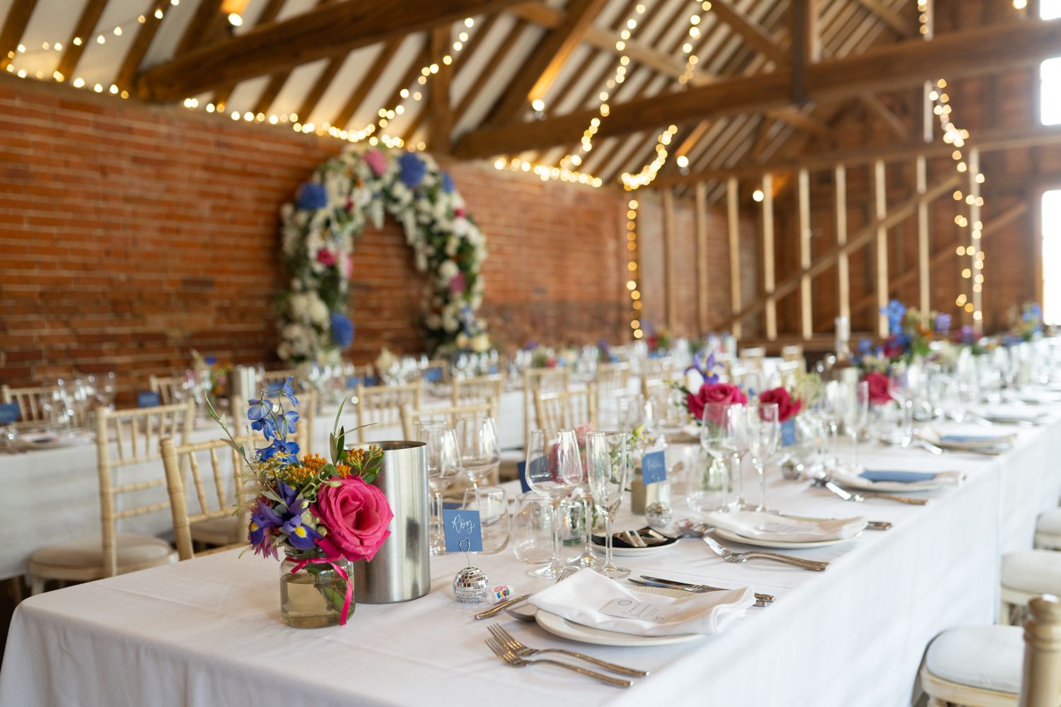 Long rustic barn reception tables decorated with elegant floral centerpieces and place settings for a wedding celebration.