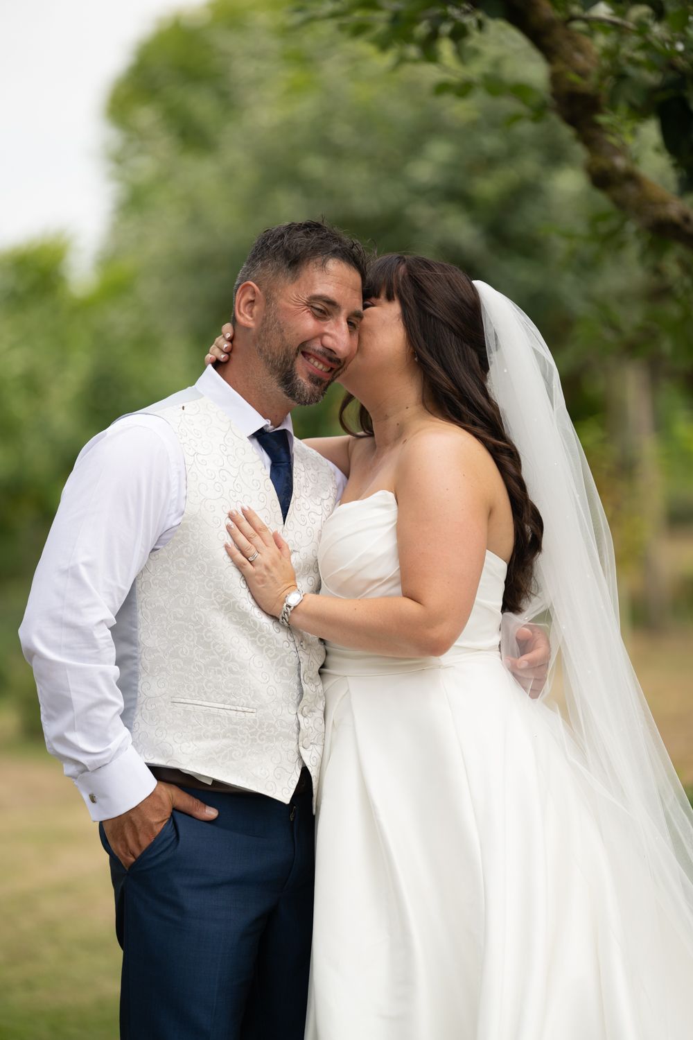A romantic moment between newlyweds in an outdoor garden setting wearing white and navy blue wedding attire.