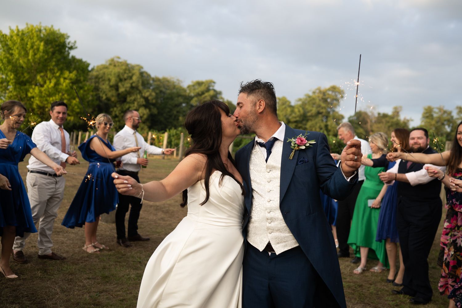 Wedding guests form a human tunnel outdoors on a grassy lawn for a celebratory exit.