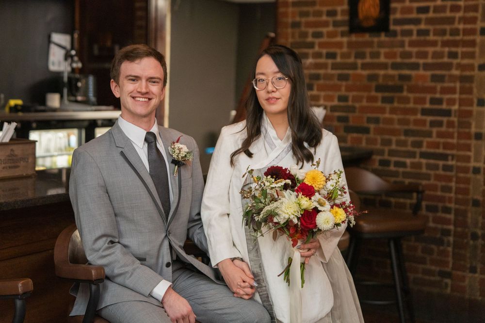 A couple shares a joyful moment during their wedding ceremony in front of a rustic brick wall backdrop.