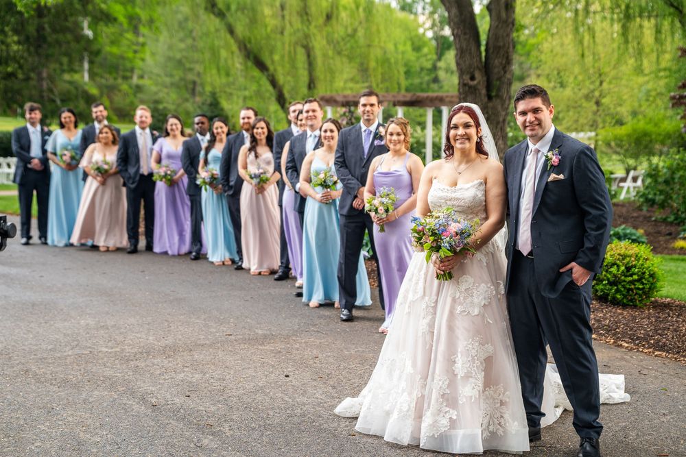 Wedding party and guests line up outdoors for formal photos in a lush garden setting during spring celebration.