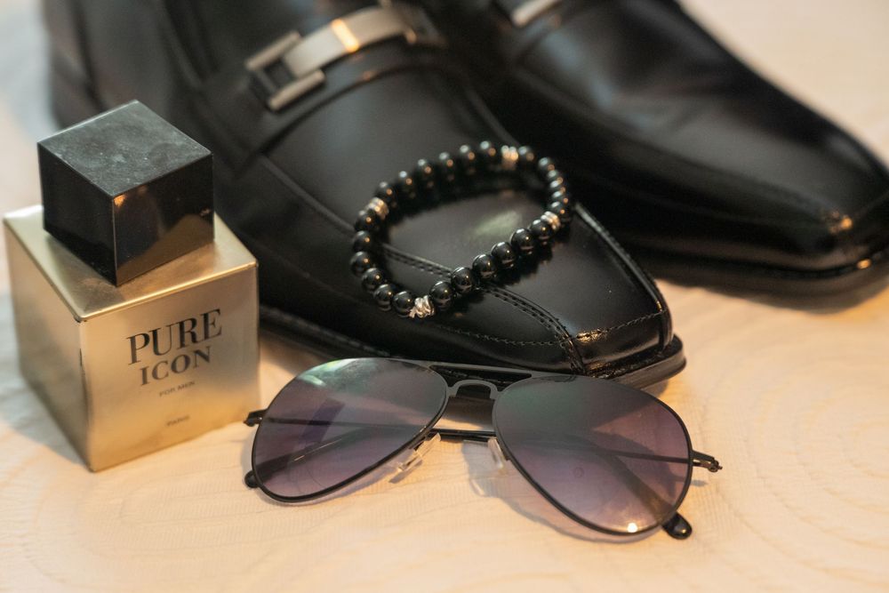 Stylish black leather accessories including sunglasses, bracelet, and shoes arranged with luxury packaging on beige surface.