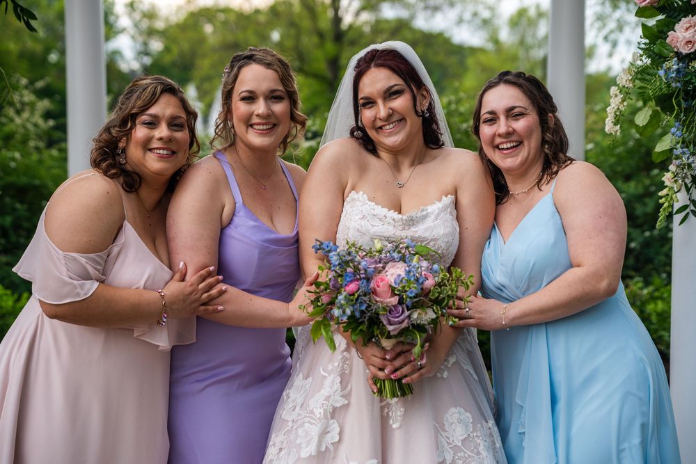 A group wearing purple and blue bridesmaid dresses pose together outdoors during a wedding celebration.