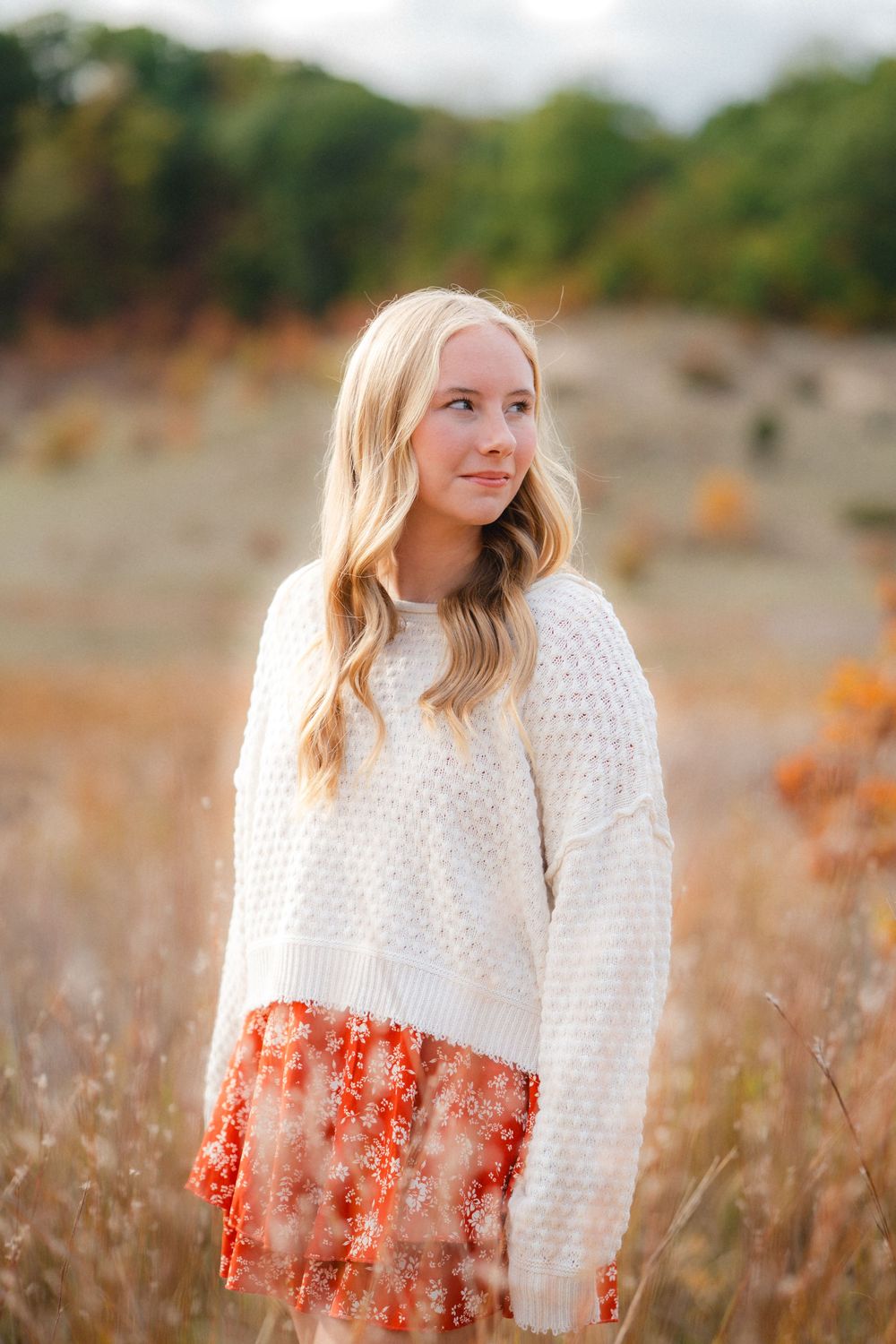 A cream knit sweater with orange floral pattern photographed in a golden autumn meadow.