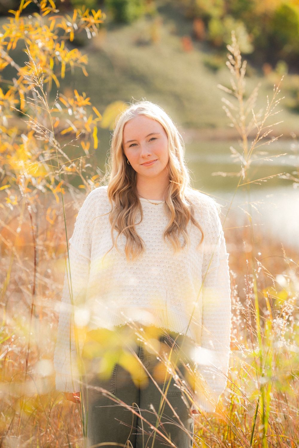 A dreamy autumn portrait in a golden field with soft sunlight filtering through yellow foliage and dried grasses.