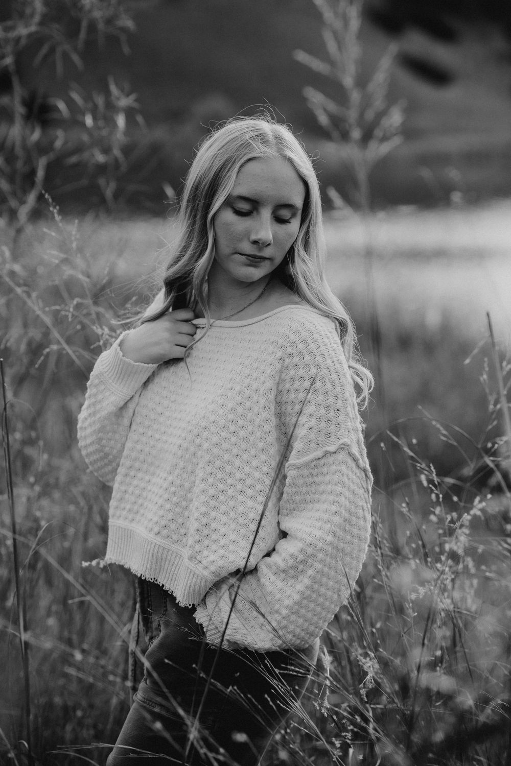 Black and white portrait series of a woman in a white knit sweater posing in a field of wildflowers.