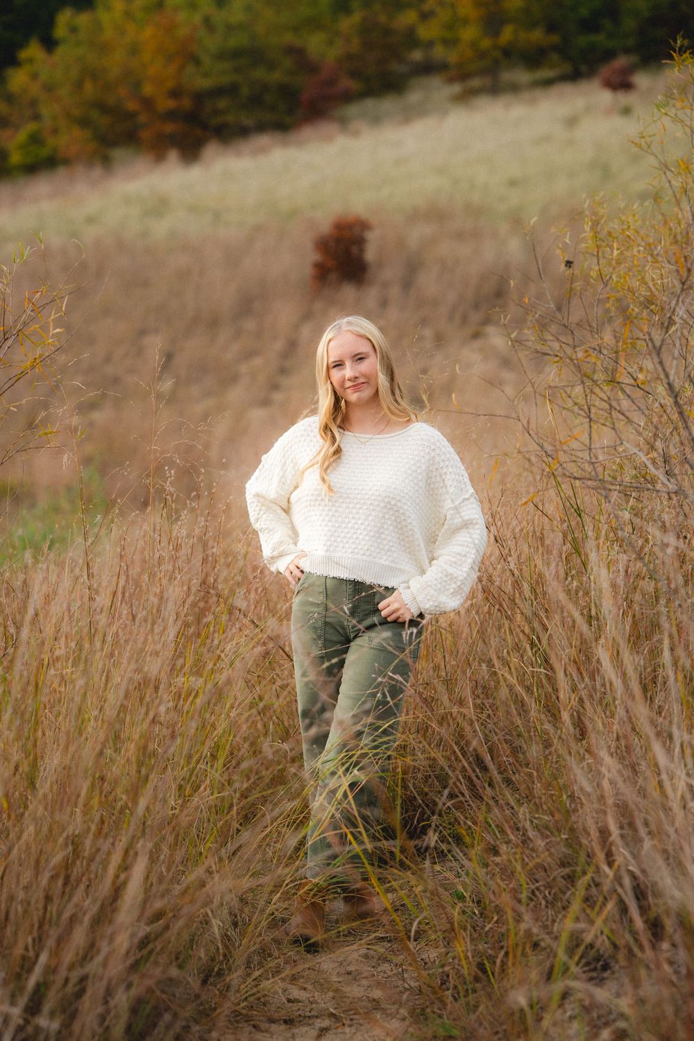White sweater and olive pants outfit styled for autumn outdoor photography in tall grass.