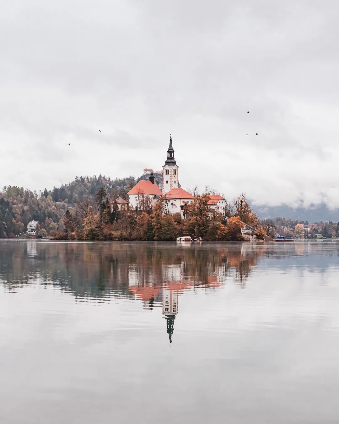 Lake Bled island with church and autumn trees reflected in calm water.