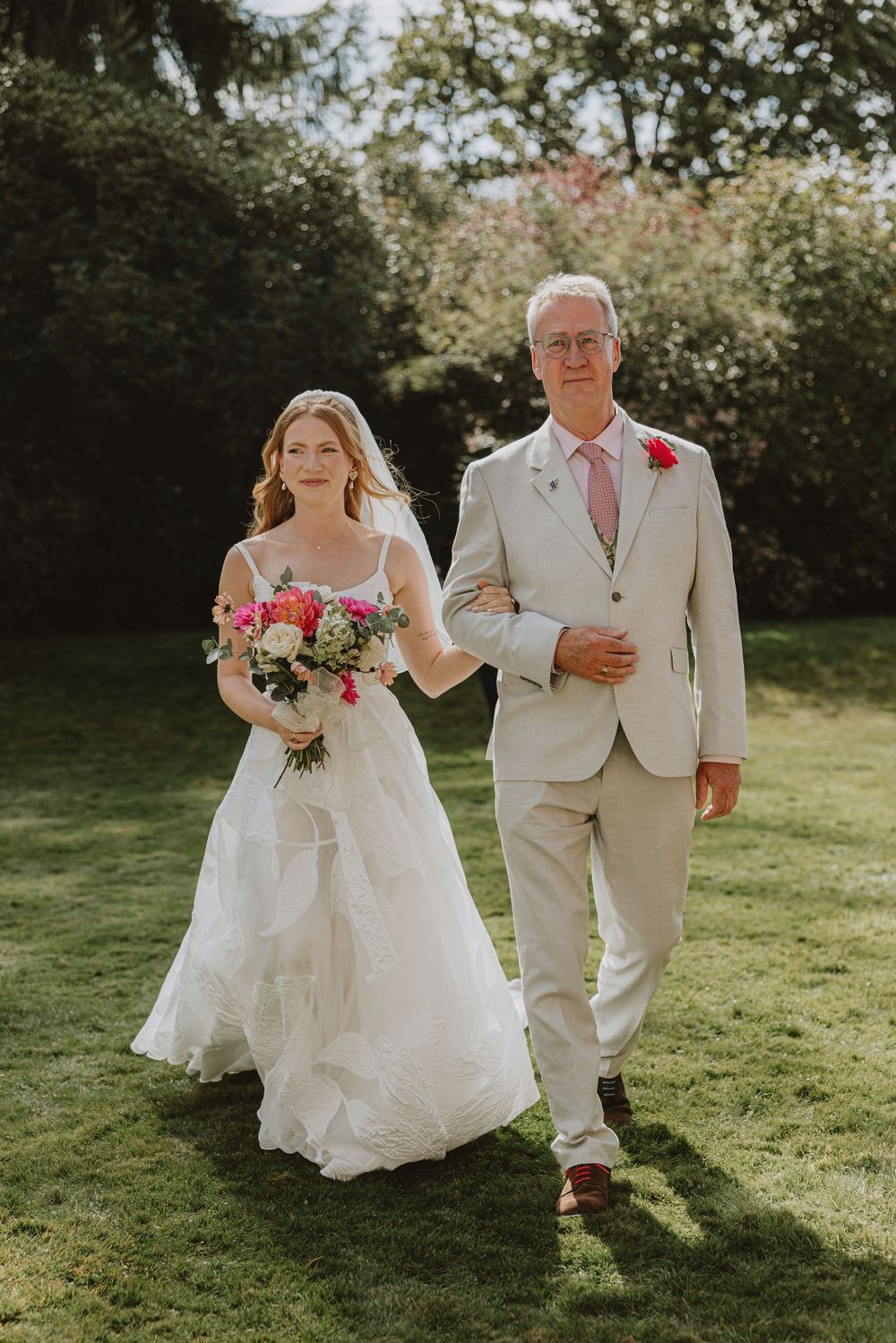 Wedding processional on grassy lawn with white dress and light colored suit.
