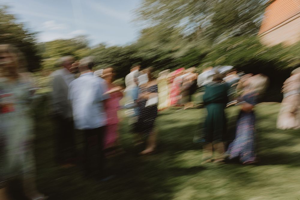 Motion-blurred image of wedding guests standing in a line outdoors on a sunny day.