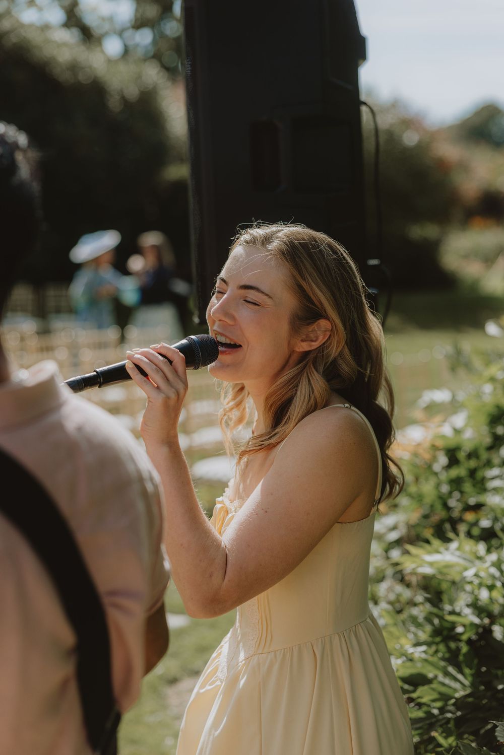 A performer in a light dress sings passionately into a microphone at an outdoor event.
