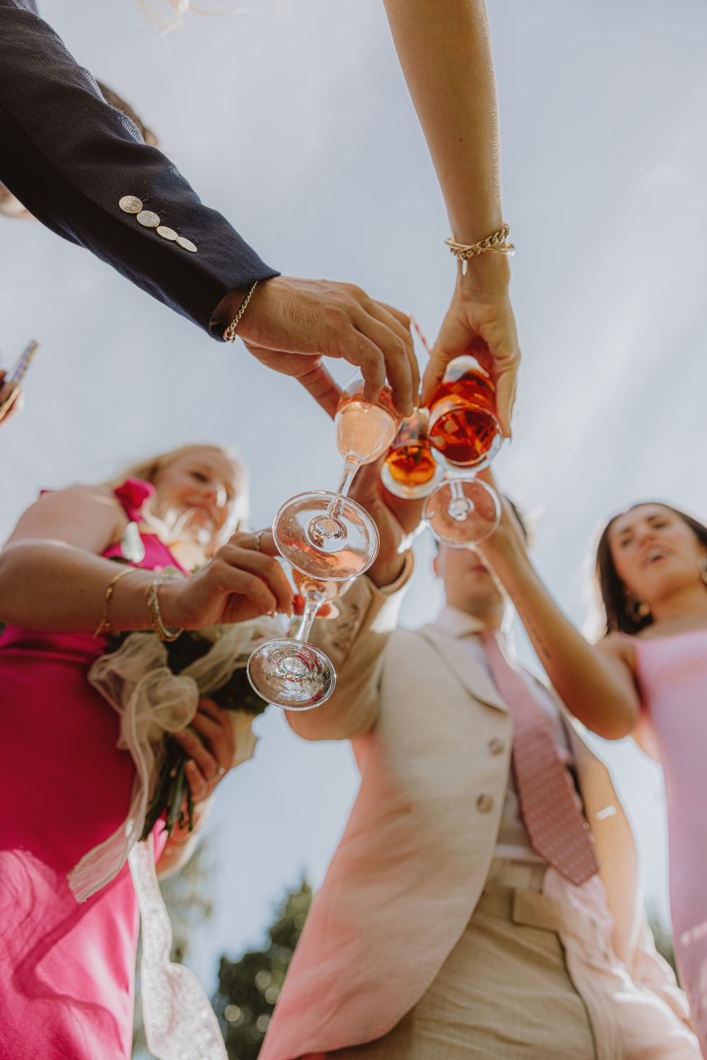 Wedding guests toasting with champagne glasses from a low angle view against blue sky.