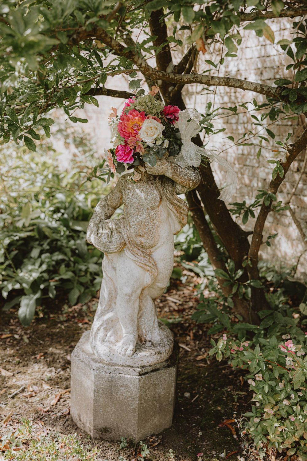Stone garden statue surrounded by blooming roses and greenery.