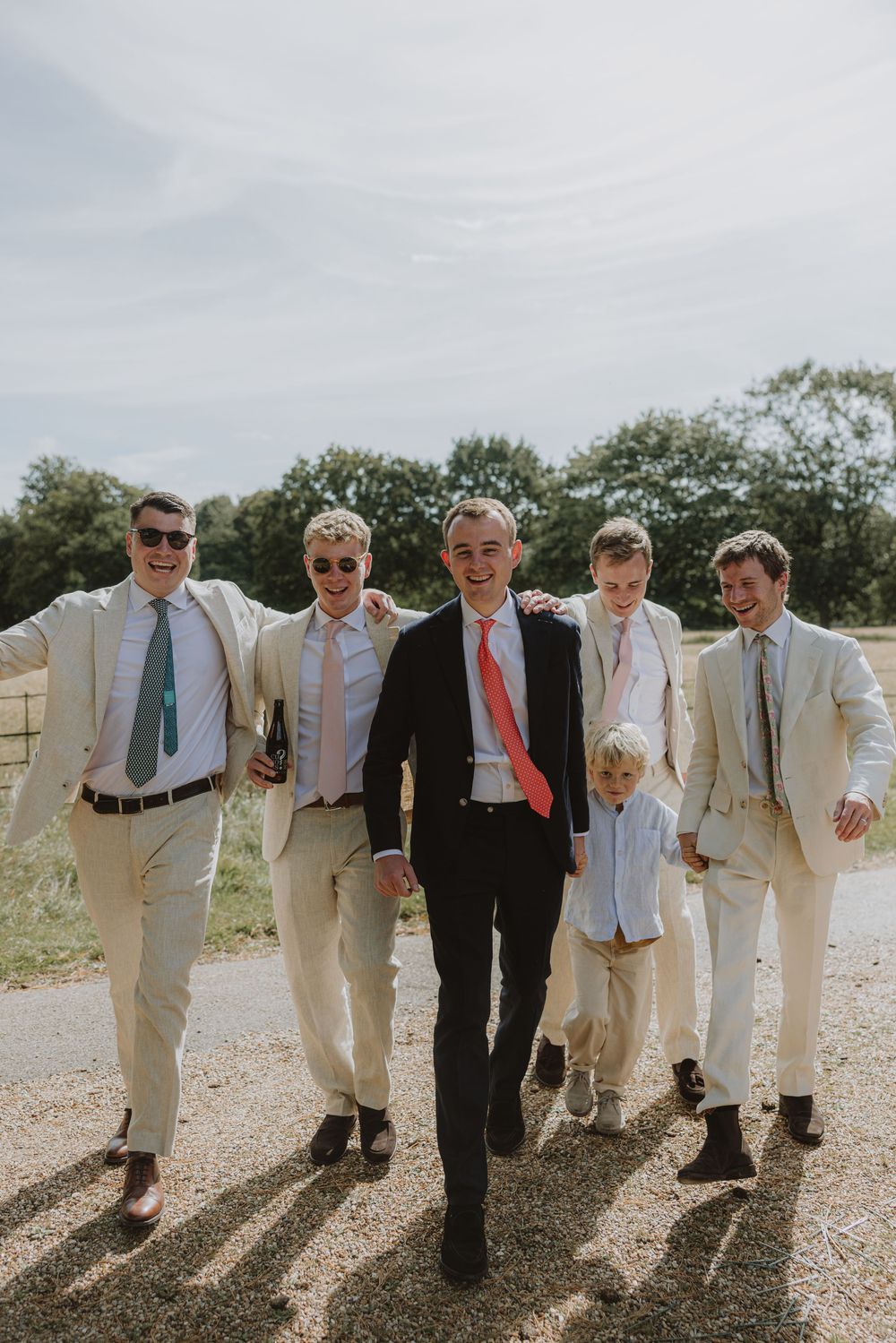 Group of groomsmen in light colored suits posing together outdoors.