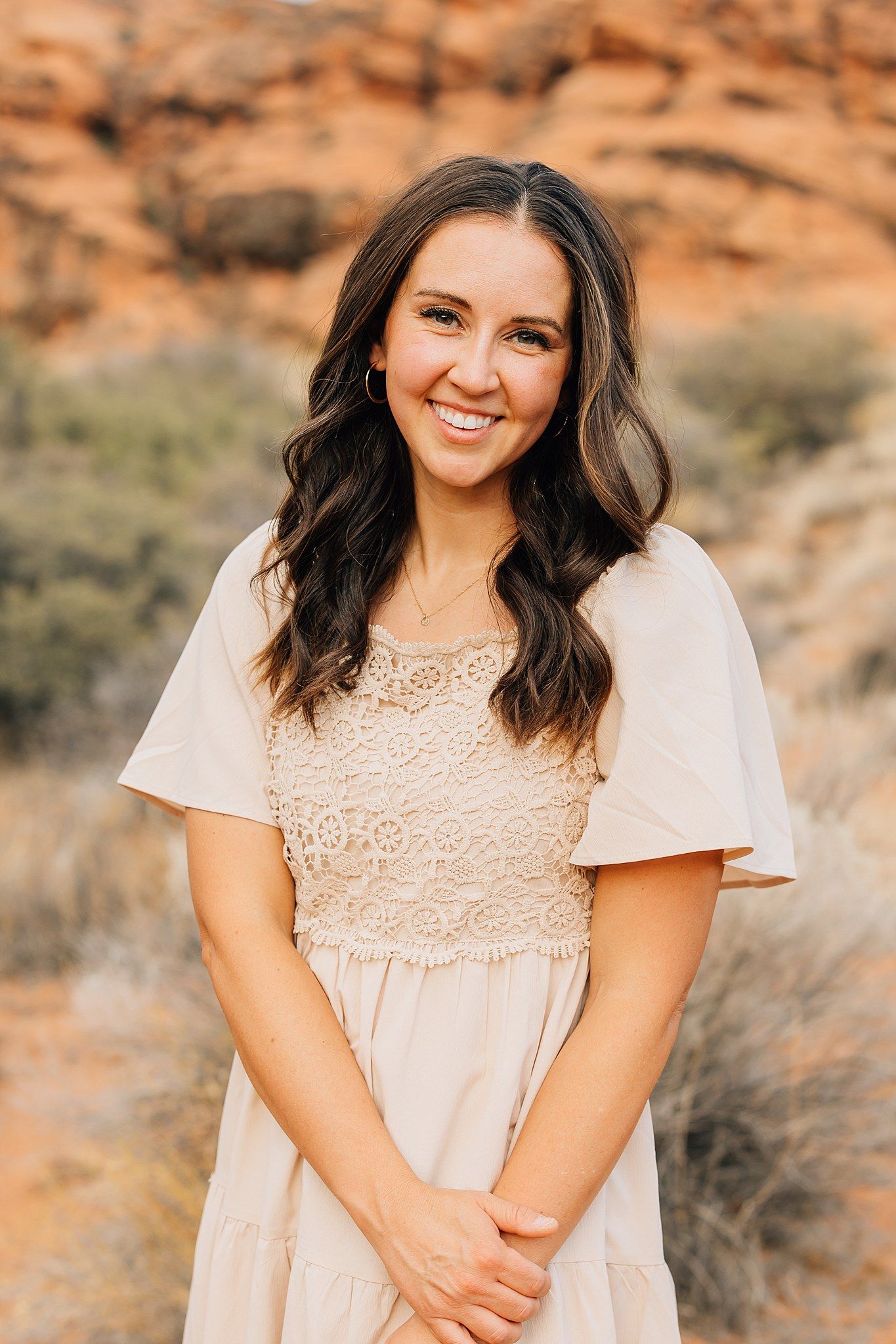 Portrait of person in white lace dress against desert backdrop at sunset.
