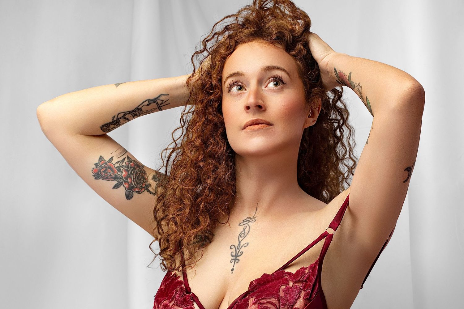 gorgeous mum of two burgundy lingerie poses elegantly with flowing red fabric against a light gray studio backdrop. classy bodiour.
