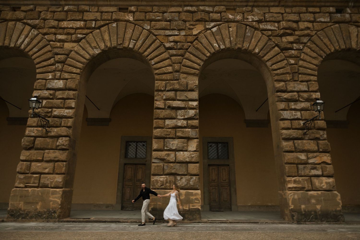 Two people in traditional white clothing walk through a stone archway in a historic Mediterranean building.