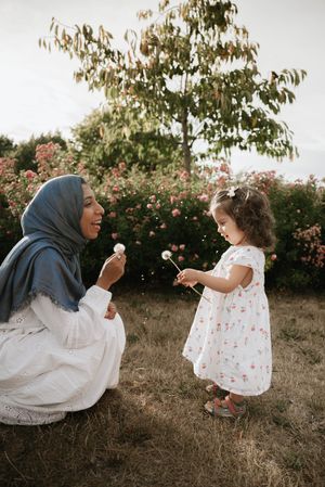 A sweet moment outdoors as two people share dandelions together in a garden with blooming flowers and trees.