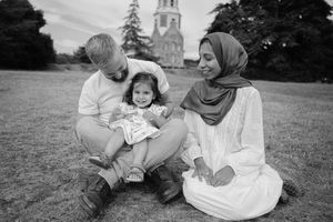 A loving family lying together on grass in a park during a sunny day, captured in black and white photography.