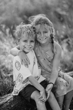 Black and white photo of two young friends sitting together outdoors with doodles drawn on their arms.