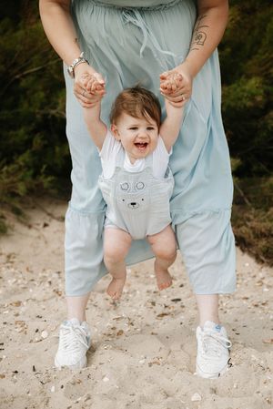 A sequence of photos showing a baby in a gray romper being lifted and swung by hands while standing on sandy ground.