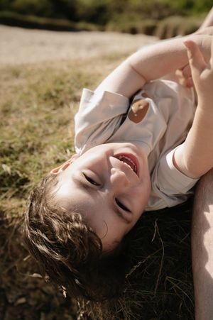 A person lies in the grass on a sunny day, laughing joyfully with closed eyes and natural lighting.