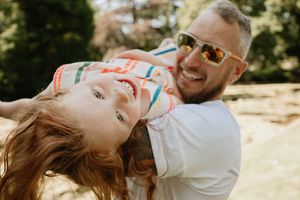 Couple laughing together while lying on the ground in a sunny outdoor setting.